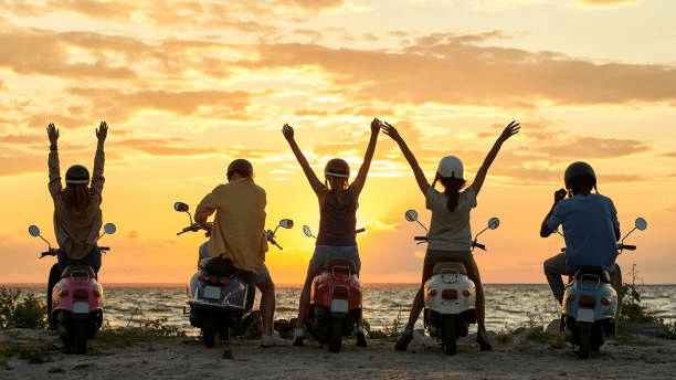 Gente feliz en moto por Formentera con la puesta de sol de fondo.