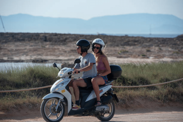 Pareja feliz en moto de alquiler por el camino de Ses Illetes en Formentera.